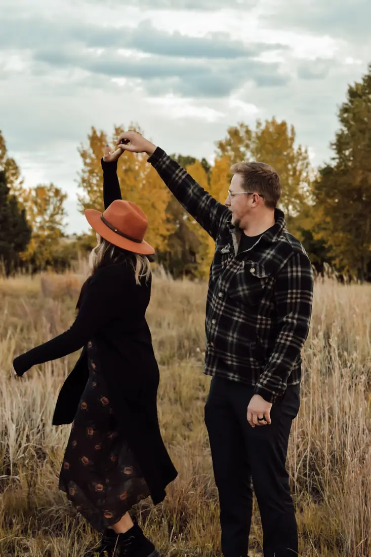 Woman in a rust hat twirling under her partner's arm in an autumn field