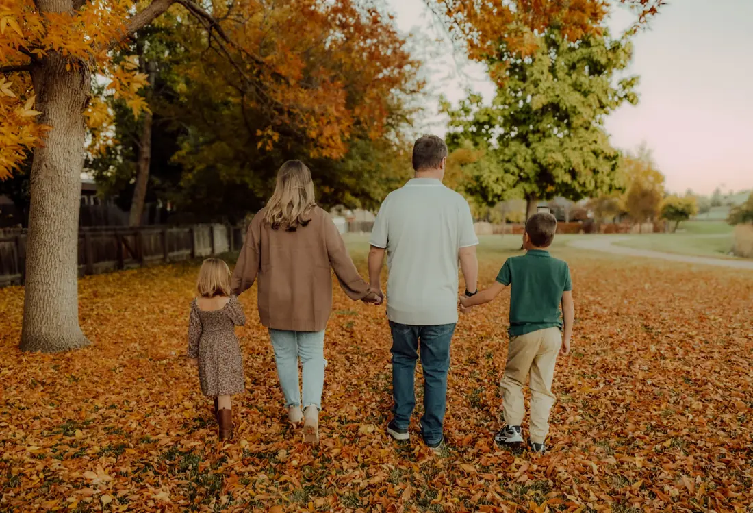 Family walking away holding hands through autumn leaves