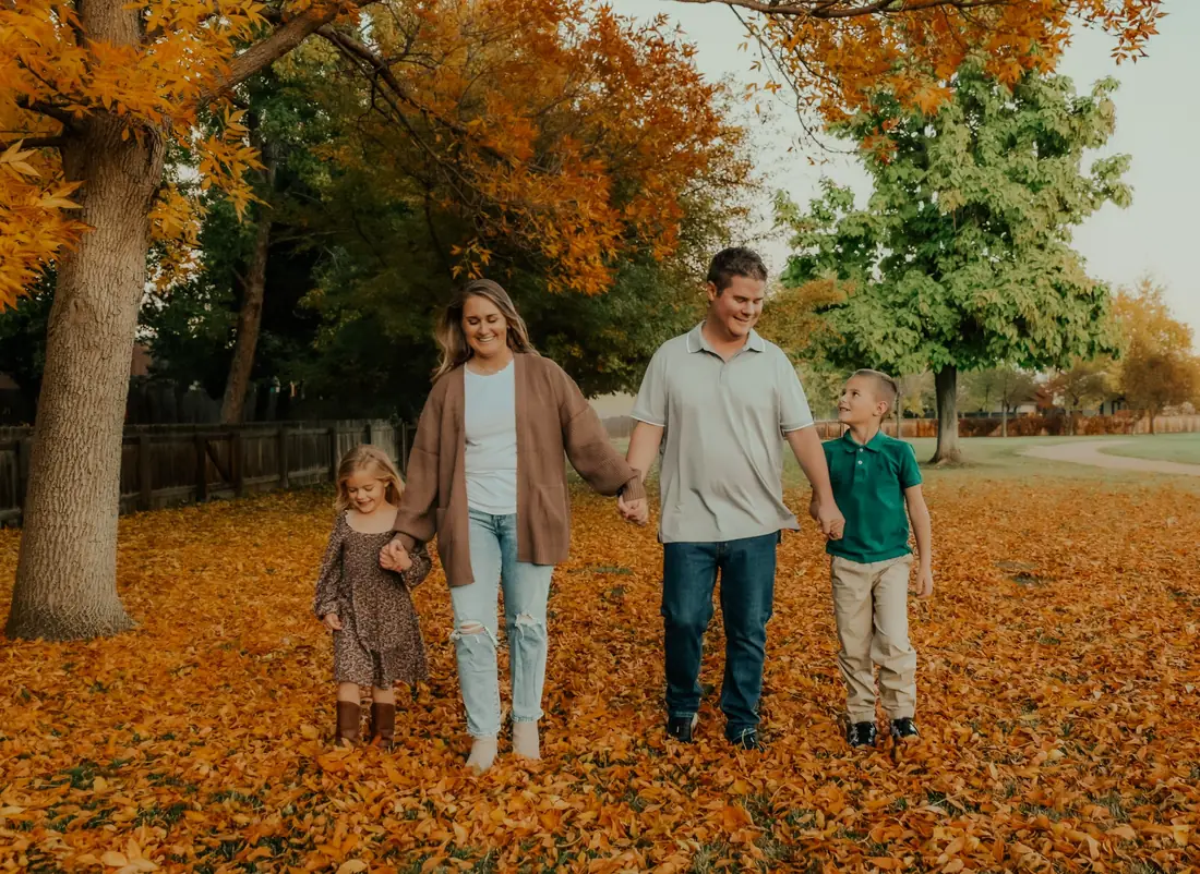 Family of four walking hand in hand through fallen autumn leaves