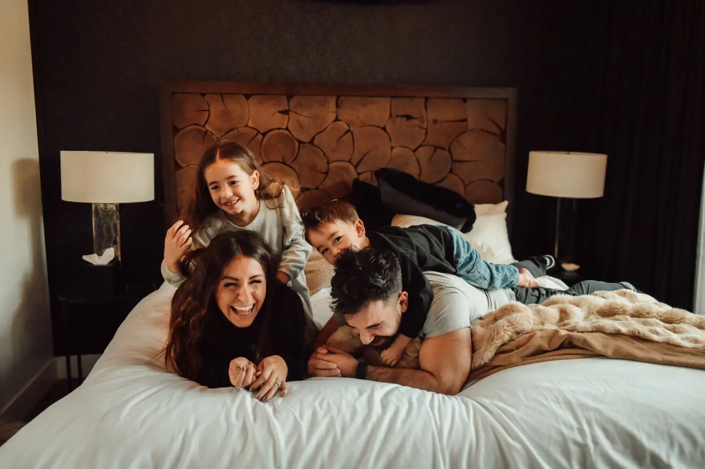 Parents and two children piling onto a bed, laughing