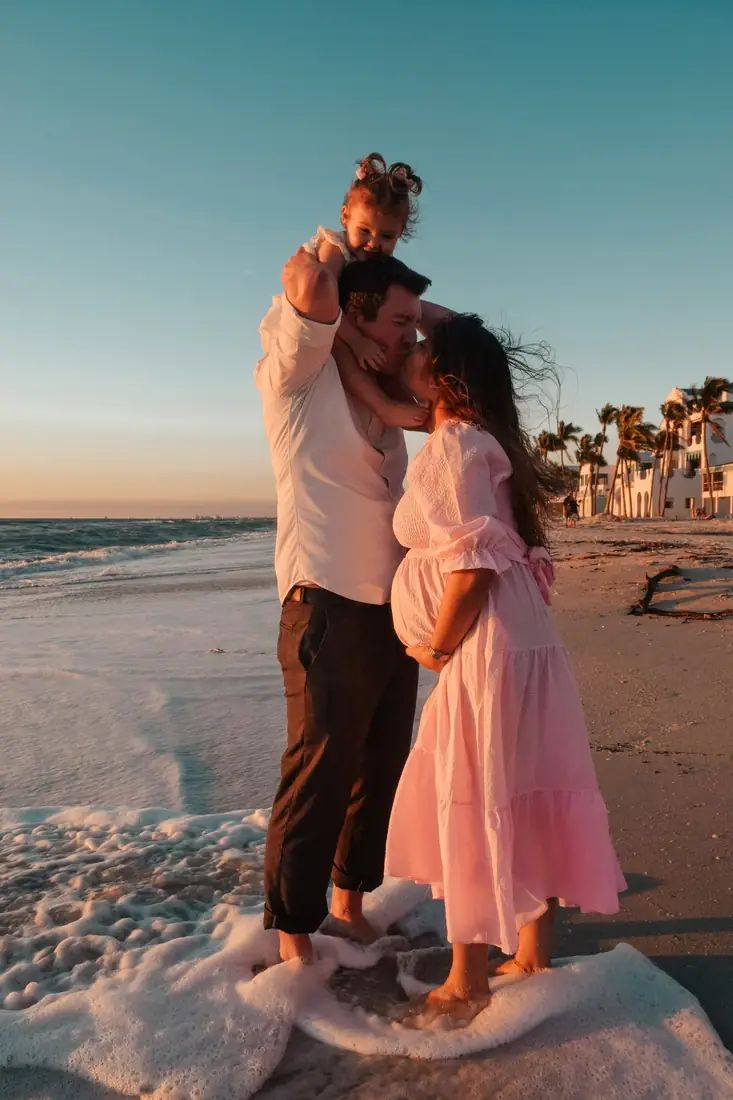 Family kissing in the surf at sunset, toddler on dad's shoulders